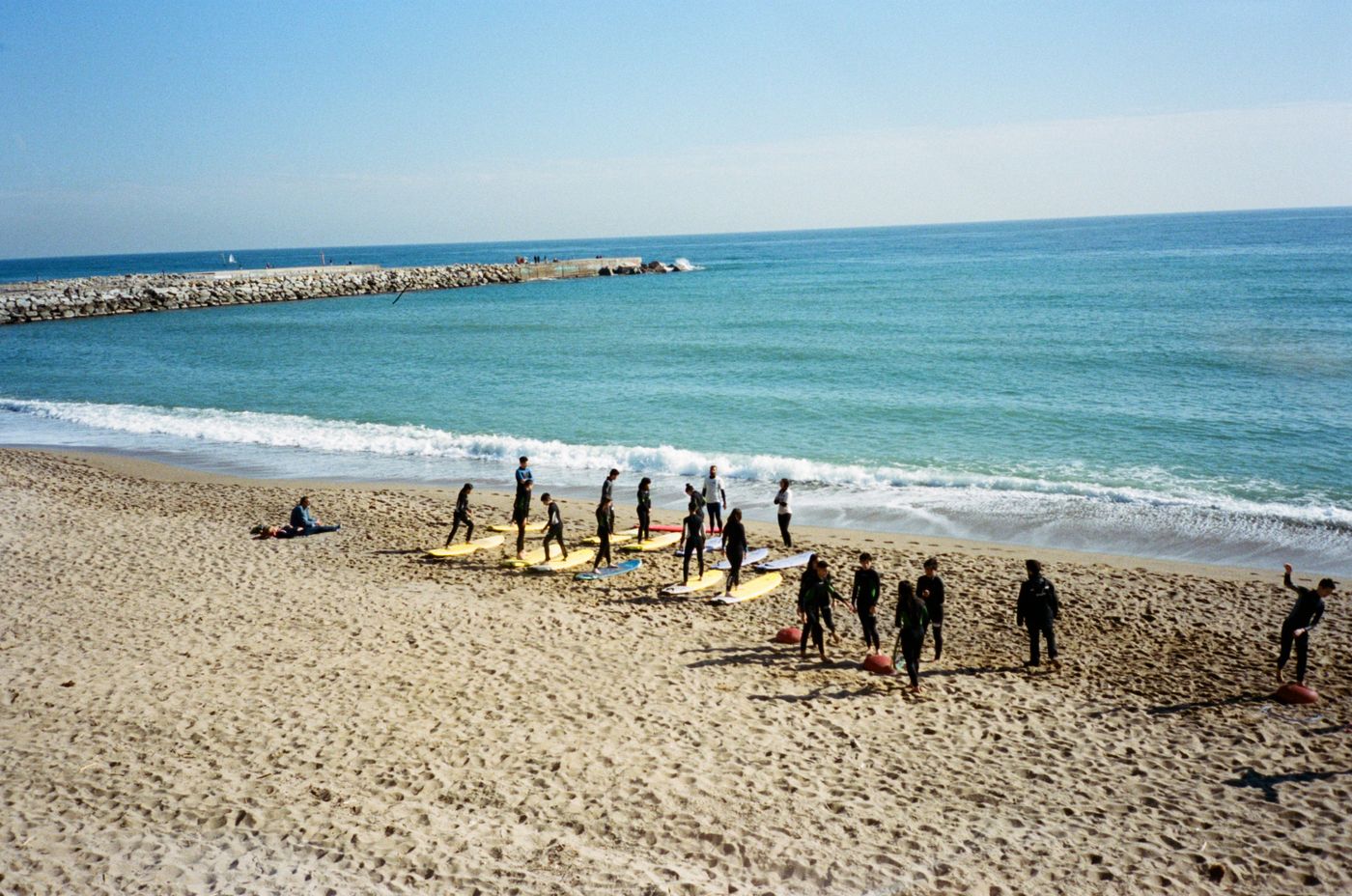 A group practises standing on surfboards arranged on a sandy beach.