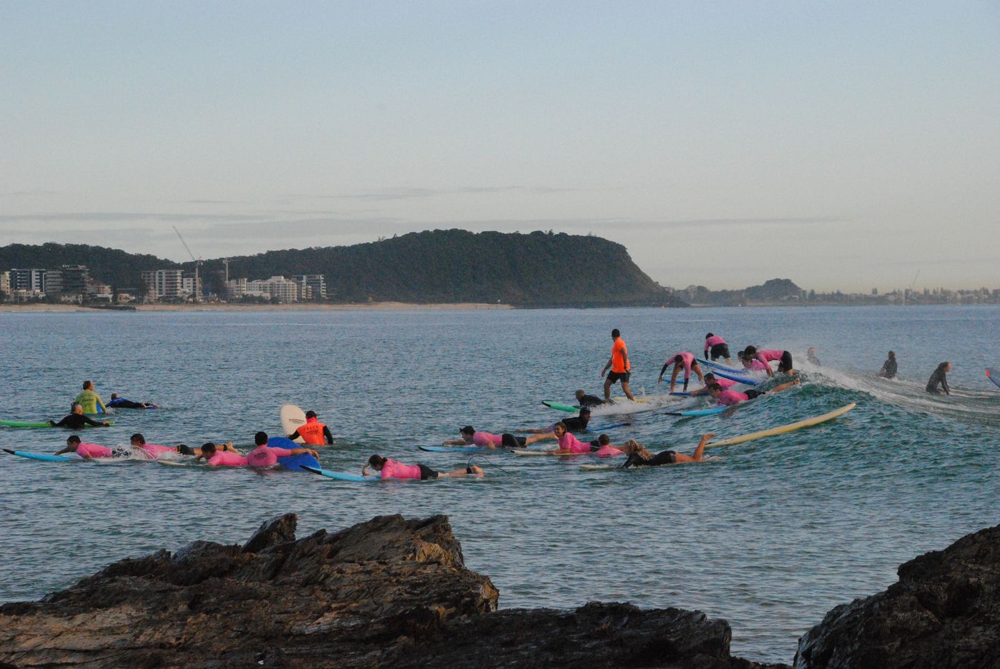 A surf lesson group floats on boards close to a coastal beach.