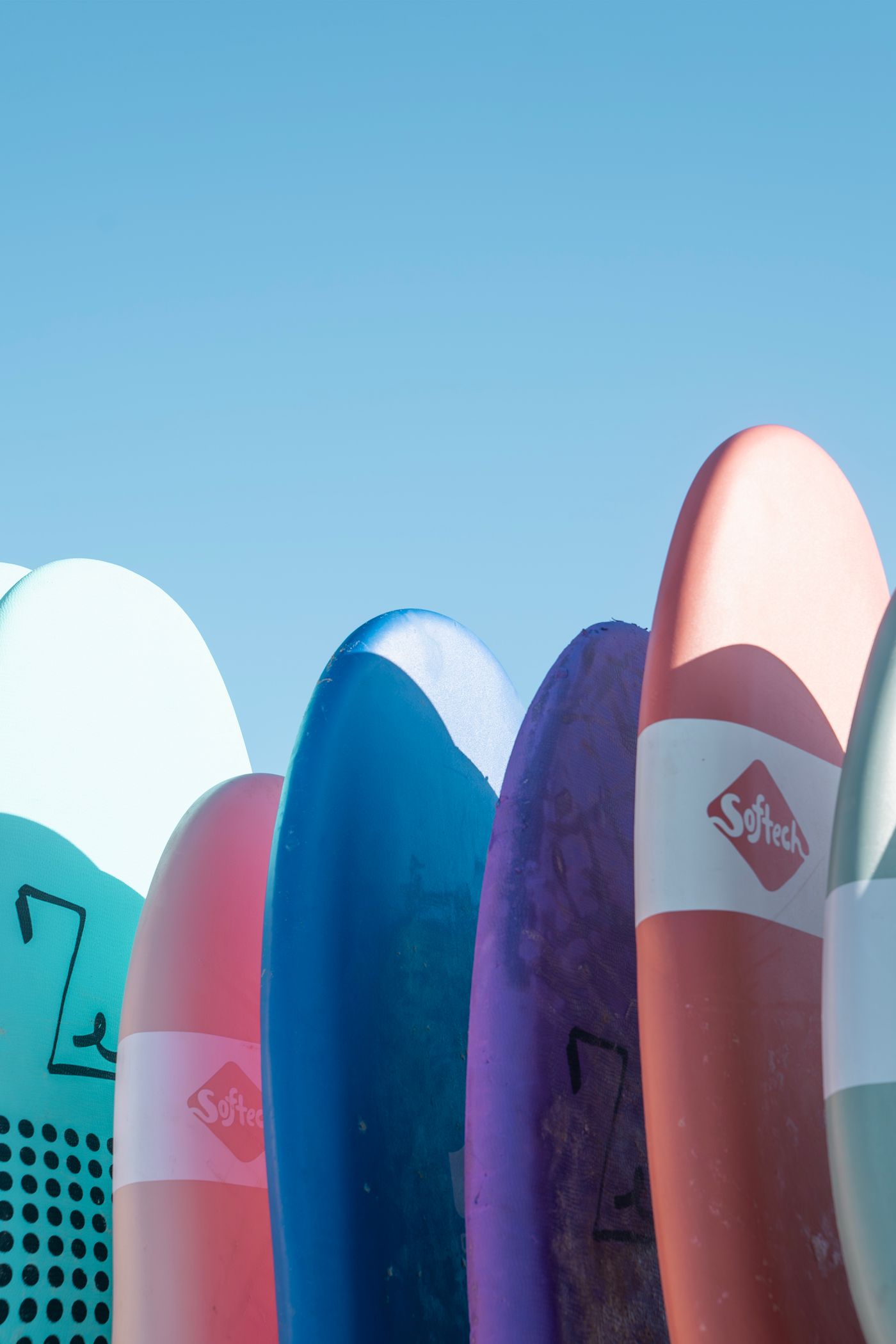 Several colourful foam surfboards stand upright in an outdoor rack.