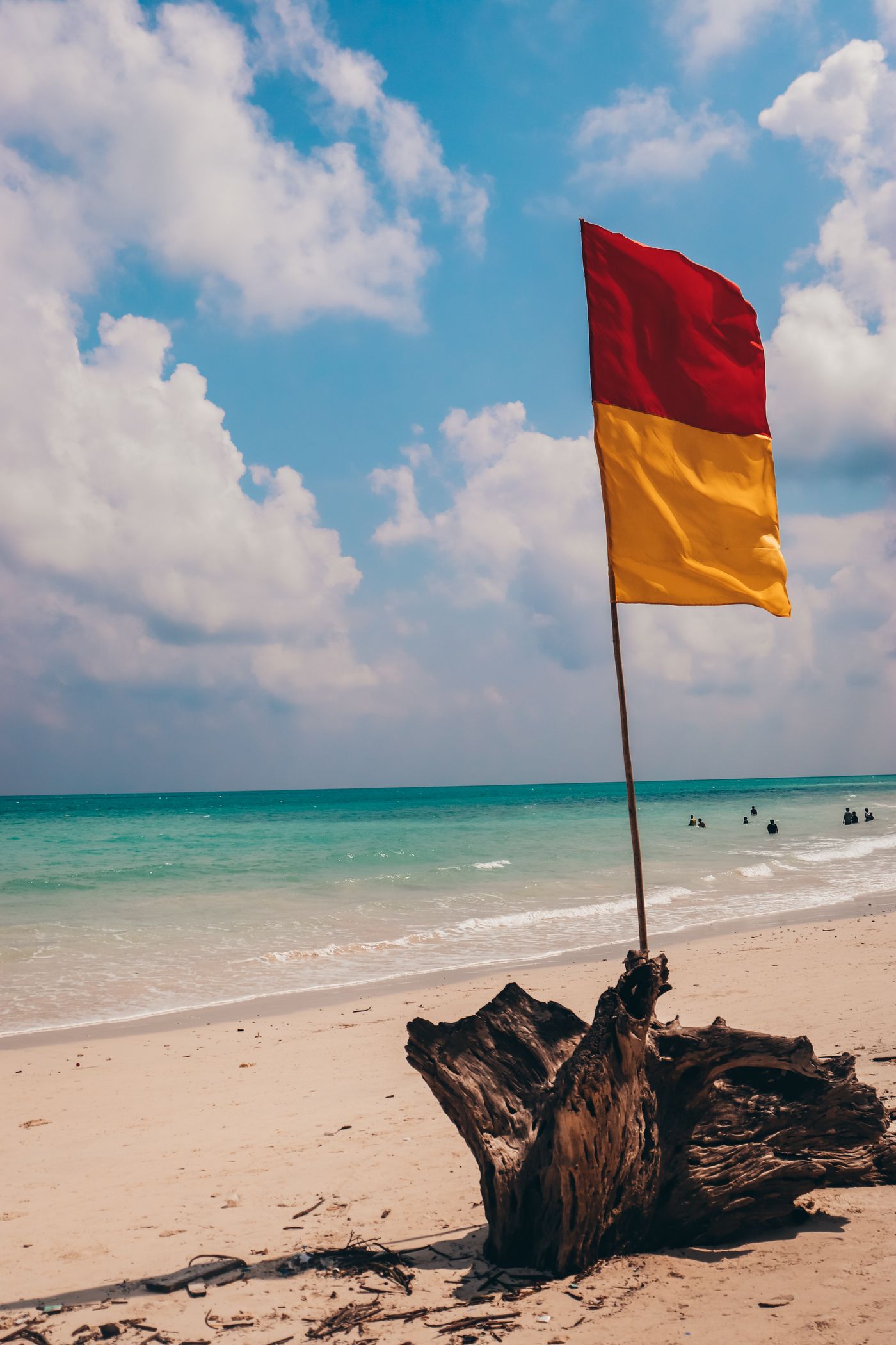 A red and yellow lifeguard flag stands on the sand near the sea.