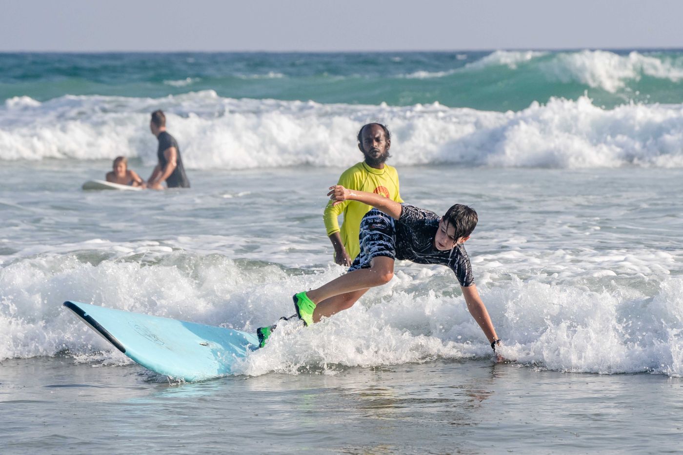 An instructor stands close to a learner practising in shallow white water.