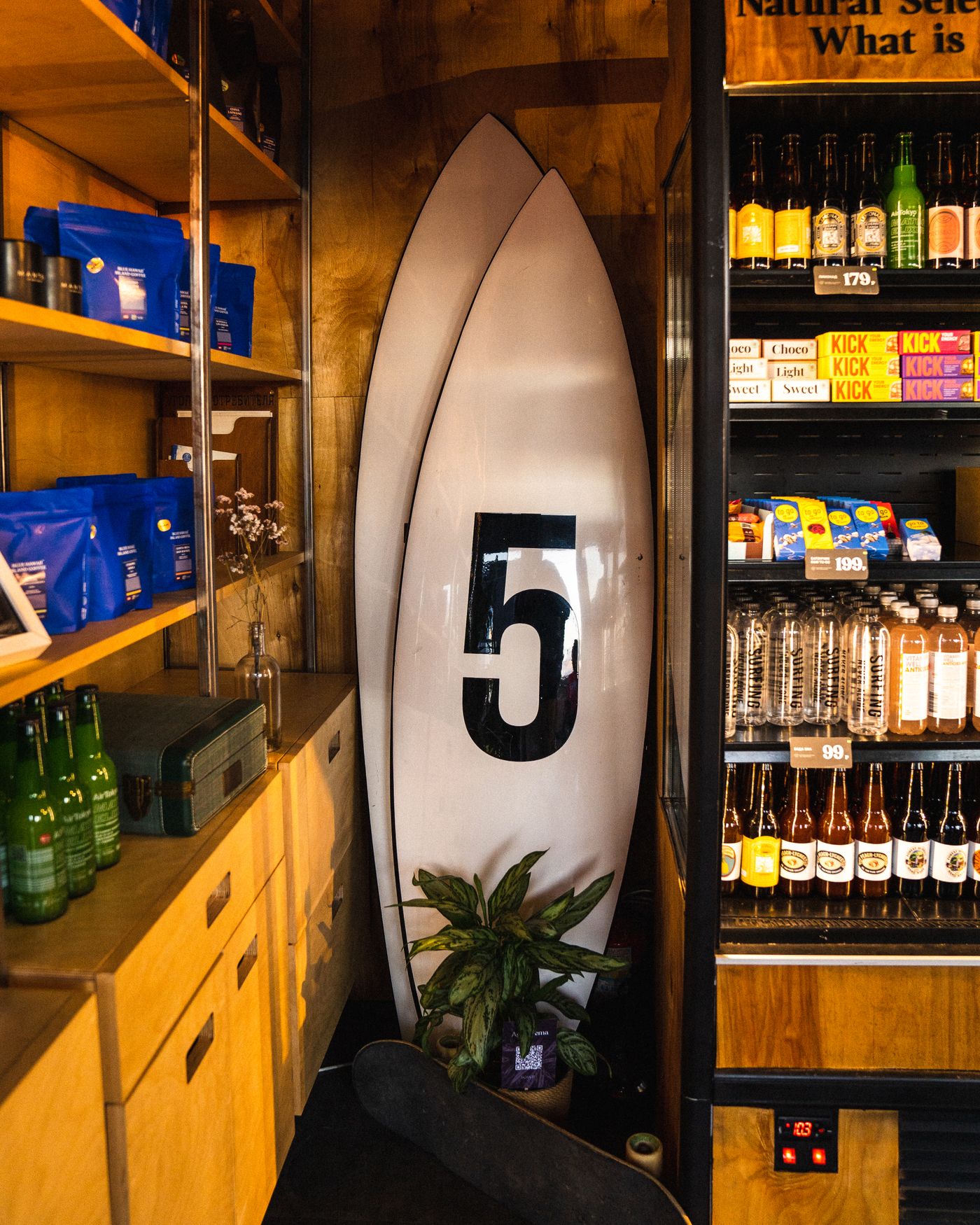 Two numbered surfboards stand among the shelves of a small shop.