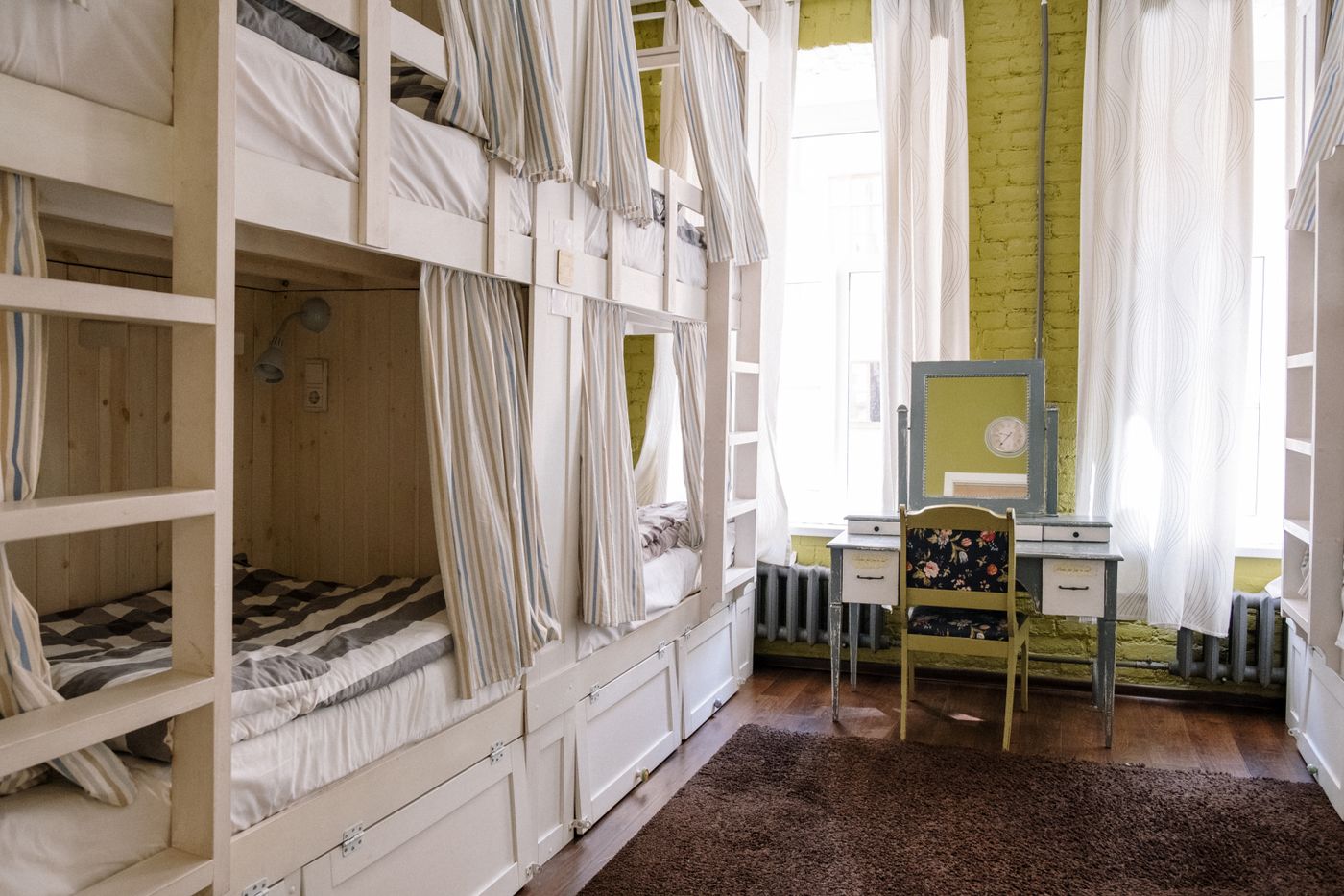 A shared hostel room has bunk beds and individual privacy curtains.