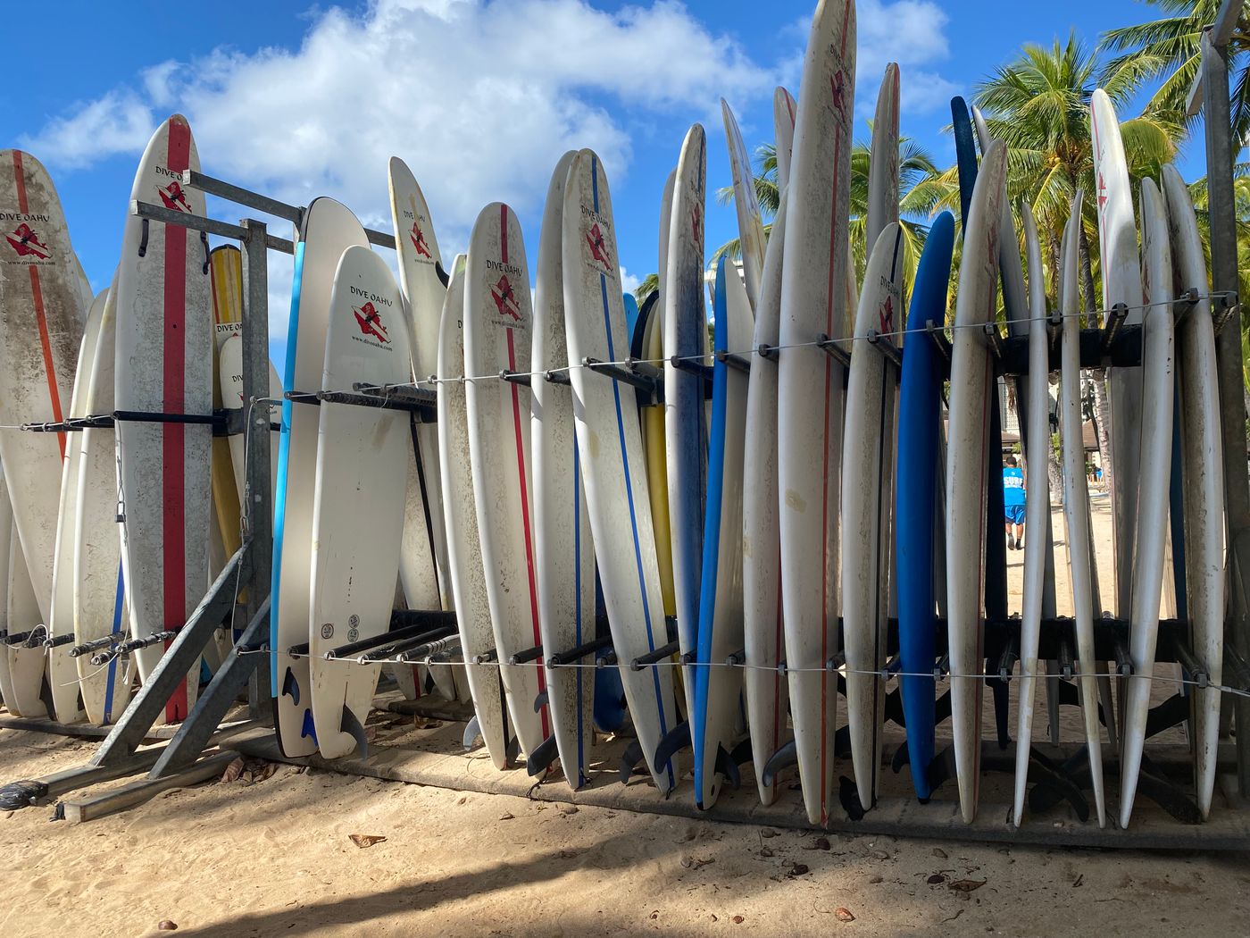 A rack holds many surfboards beside a beach under a blue sky.