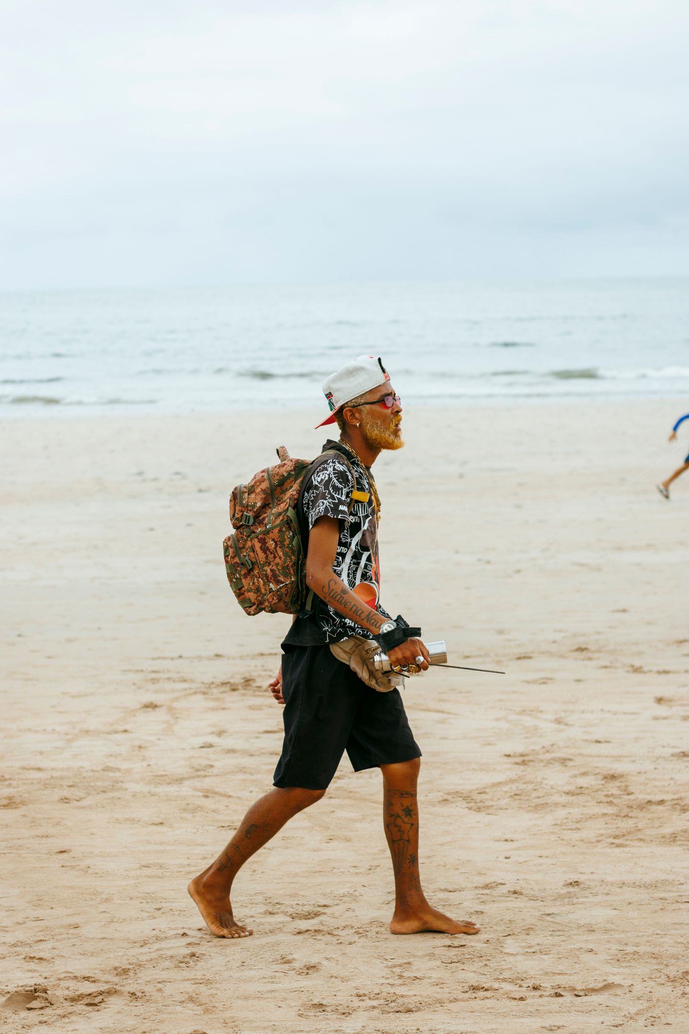 A traveller walks barefoot along the beach carrying a backpack.